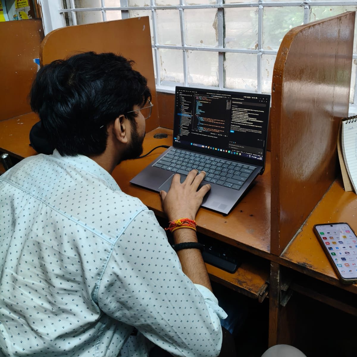 SoftFYR developer writing code on a laptop by the window